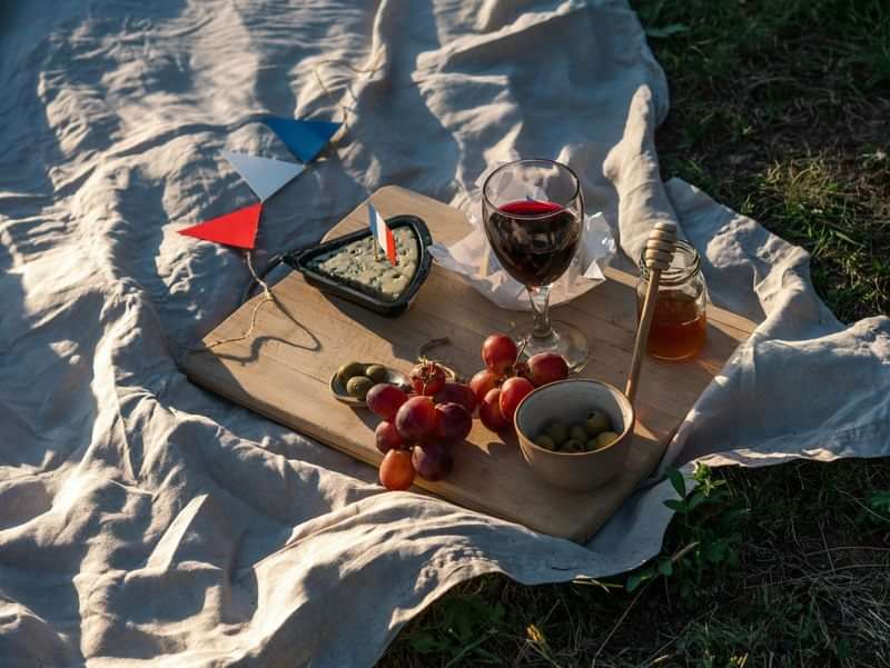 French picnic with wine, grapes, cheese, olives, honey, and decorations.