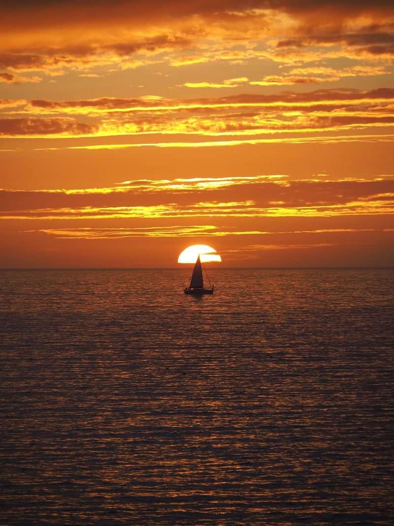 Sunset voyage: sailboat glides across calm waters under vivid orange skies.