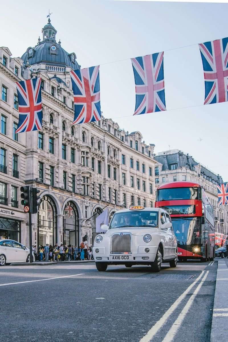 Dubbeledekkerbus en taxis in een straat met Britse vlaggen.