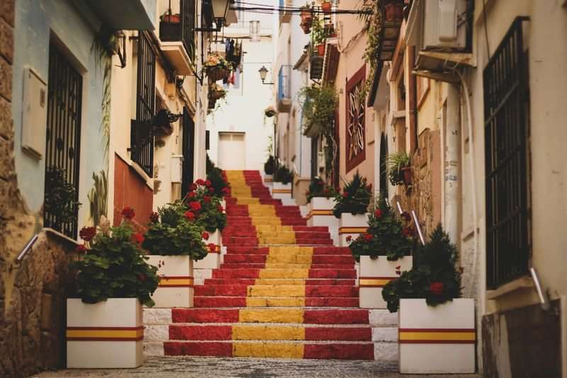 Kleurrijke trap in een schilderachtige straat vol bloemen en planten.