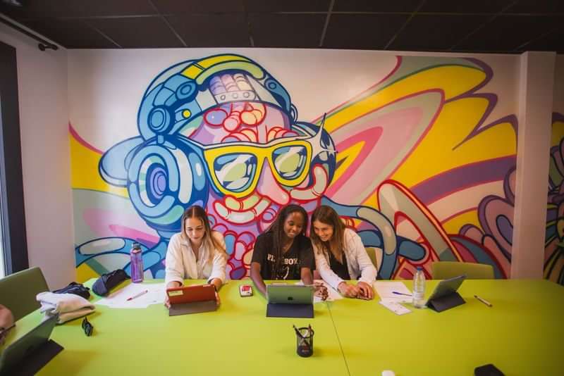 Students studying together with colorful mural in language travel classroom.