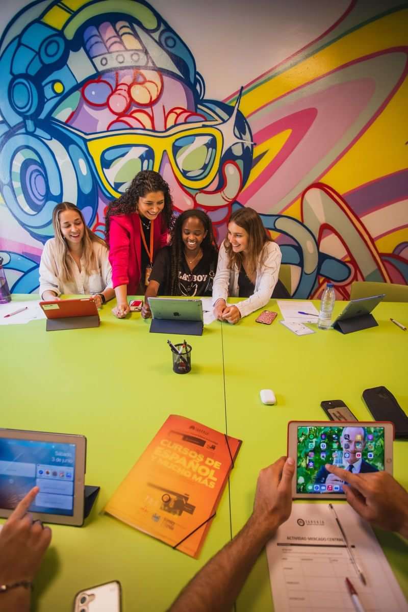 Studenten werken samen aan tablets en boeken in een kleurrijke klasruimte.