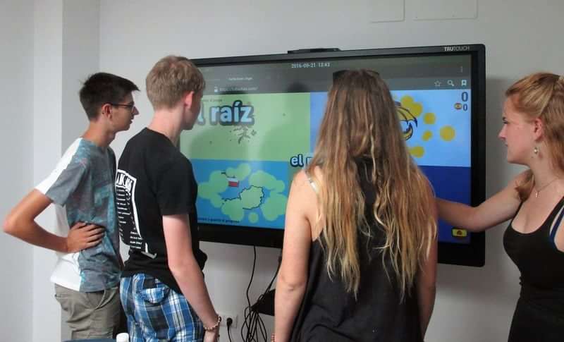 Students using interactive display for language learning, travel-themed educational activity.