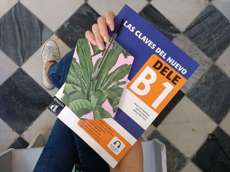 A person holding a Spanish DELE B1 exam preparation book.