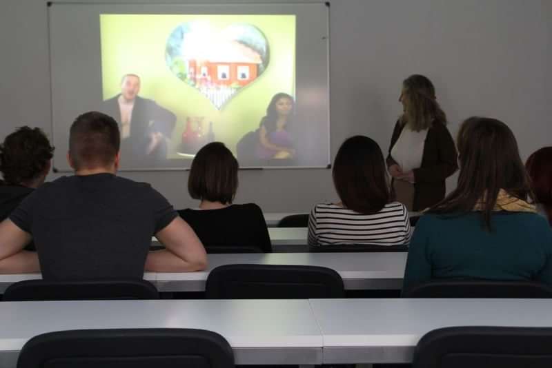 Studenten kijken naar een presentatie over talen en reizen in een klaslokaal.