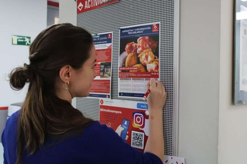 Woman reading multilingual travel and food advertisements on a bulletin board.
