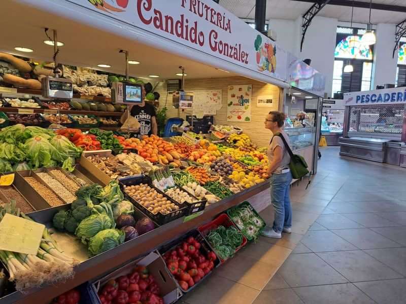 Persoon winkelt bij een groenten- en fruitkraam in een Spaanse markt.