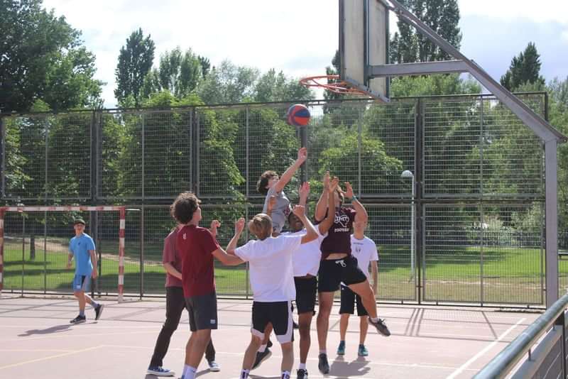 Groep jongeren speelt basketbal op een buitenveld tijdens taalreis.