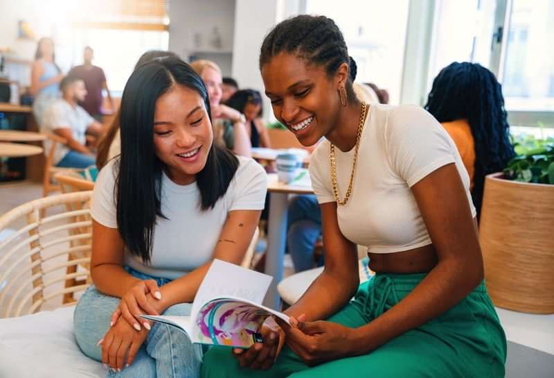 Two women discussing travel information from a brochure in a cafe.