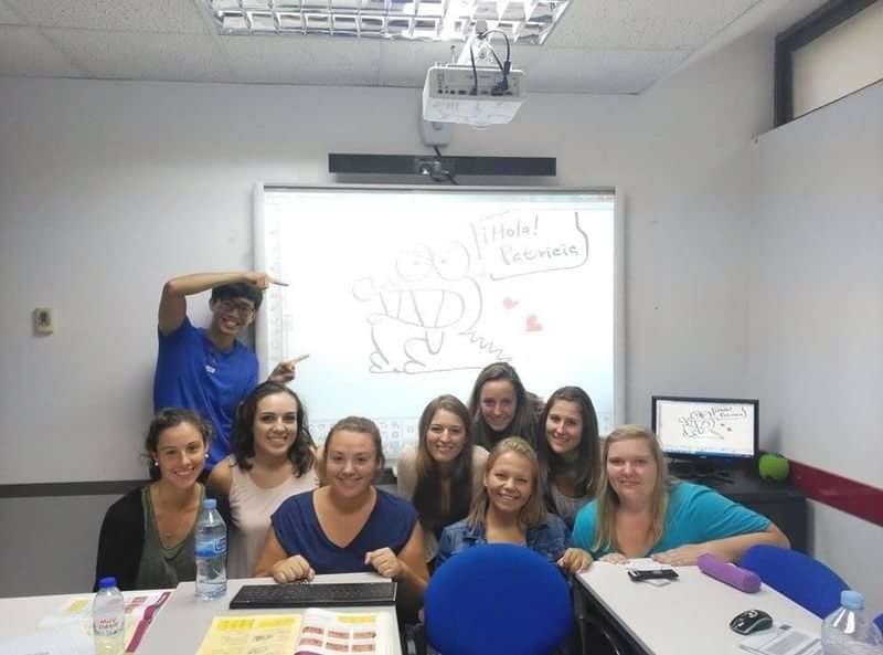 Language class group photo with "Hola! Bienvenidos" on whiteboard.