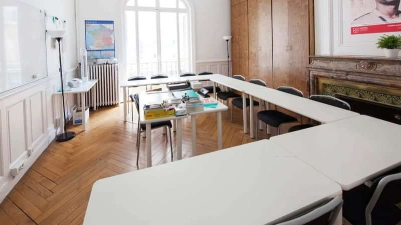 Leslokaal voor taalstudie, witte tafels, stoelen, kaarten aan de muur.