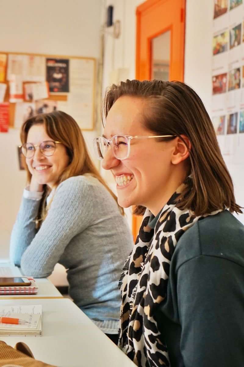 Twee vrouwen glimlachen tijdens een taallesson in een klaslokaal.