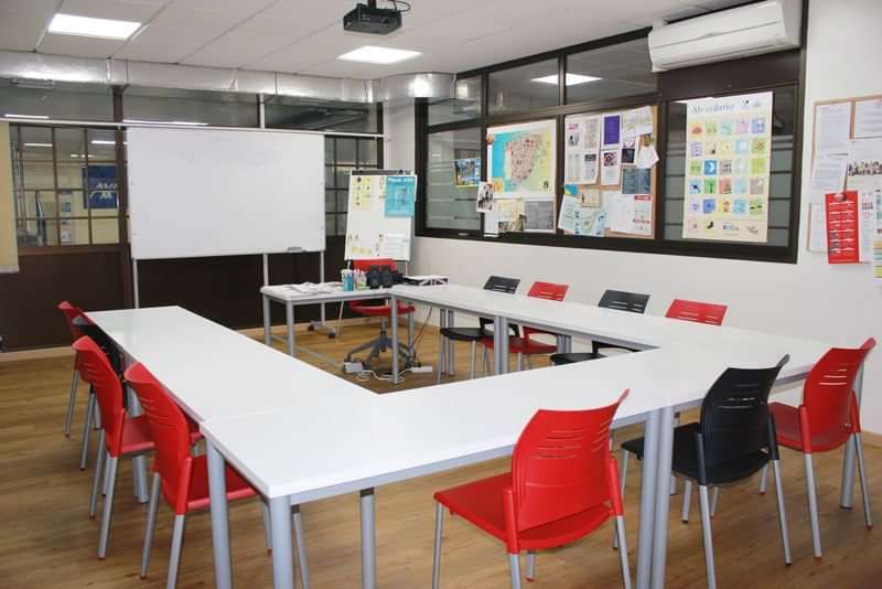 Taalreis klaslokaal, met whiteboard, wereldkaarten en kleurrijke stoelen.