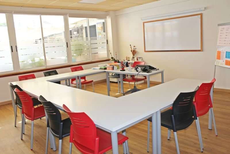 Leslokaal voor taallessen, met tafels in U-vorm en een whiteboard.