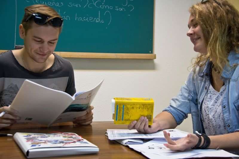 Twee mensen studeren in een taalklas met boeken en woordenboeken.