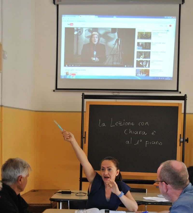 Classroom with a blackboard, student pointing at screen showing a video.