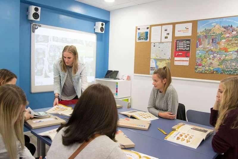 Taalreis klaslokaal met studenten en lerares, educatief materiaal in gebruik.