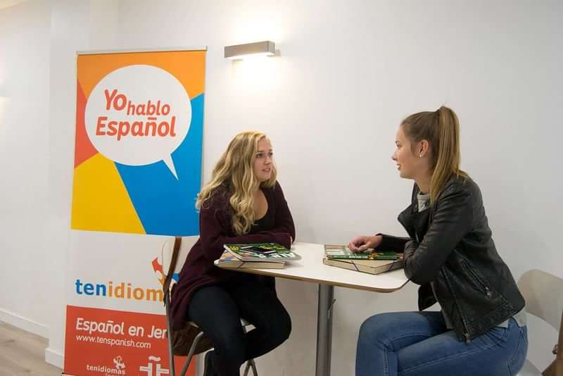 Two women conversing in Spanish next to a language school banner.