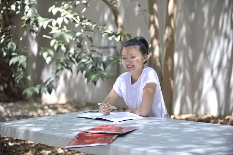 Student studeert buiten, voorbereidend op taalreis, met studieboeken.