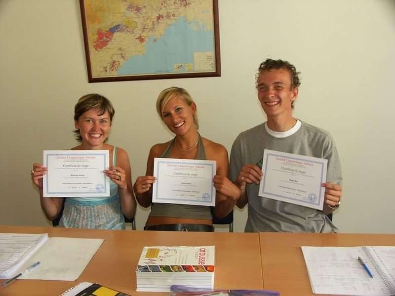 Students proudly displaying language course completion certificates in a classroom.
