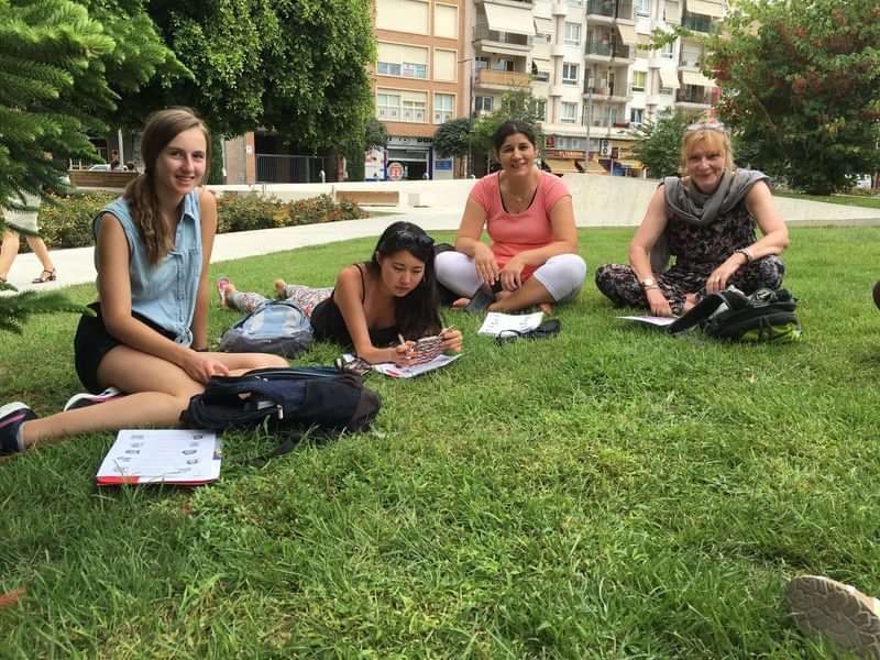 Students practicing language outdoors, studying and writing in notebooks.