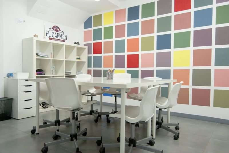Spaanse taalschool klaslokaal, kleurrijke muur, tafels, stoelen en kasten.