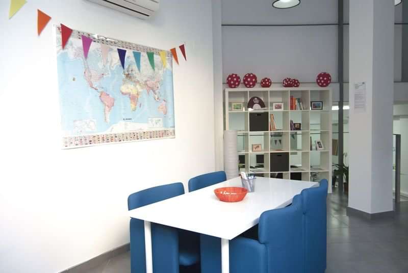 Tafel met stoelen, wereldkaart, feestelijke vlaggen, studieruimte voor taallessen.