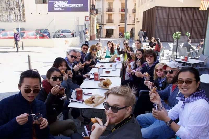 Groep internationale studenten geniet van koffie en hapjes op een terras.