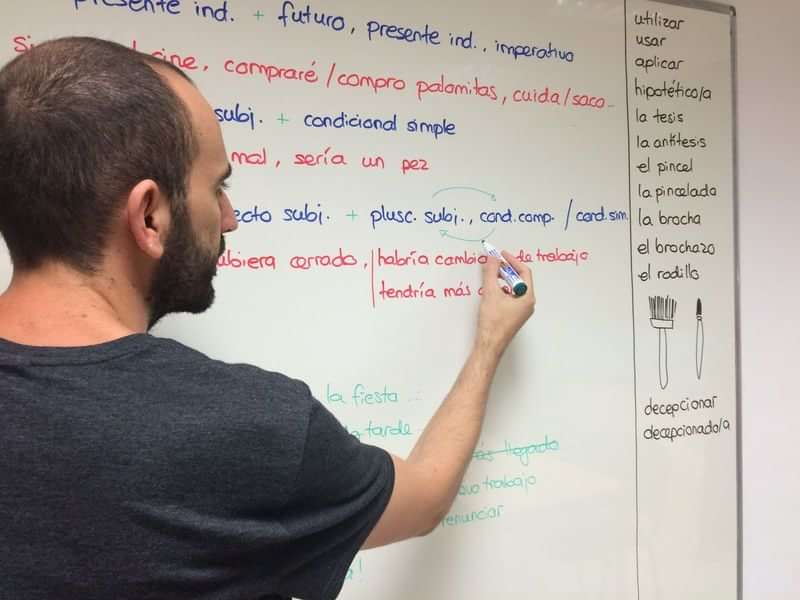Spanish language teacher writing conjugations on a classroom whiteboard.