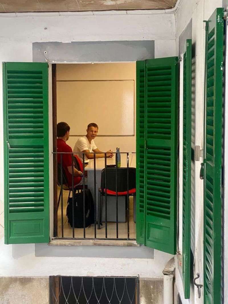 Students in a language class through open shutters, conversing and learning.