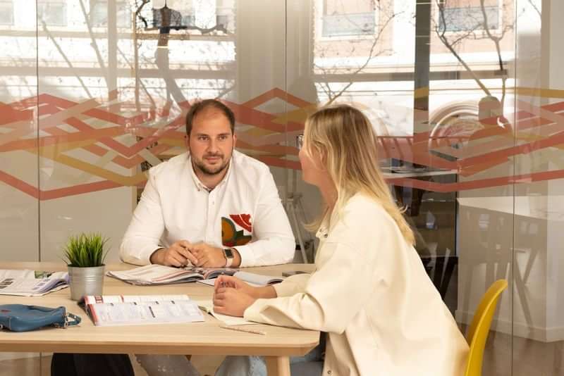 Two people discussing language travel plans in an office.