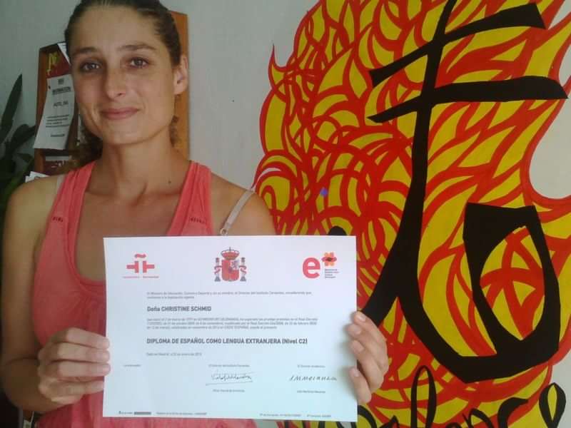 A woman holding a Spanish language proficiency certificate, smiling.