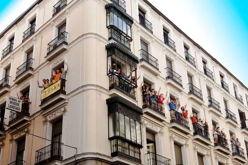 A lively language school building with students waving from balconies.