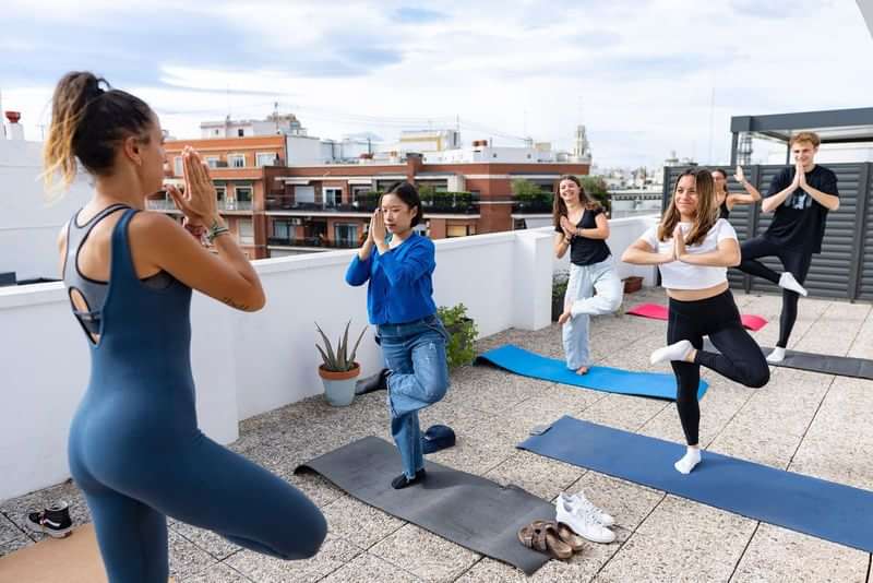 Mensen doen yoga op een dakterras, mogelijk een taalklasactiviteit.