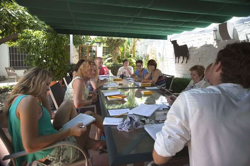 Language learners engaged in an outdoor class, books and notes on table.