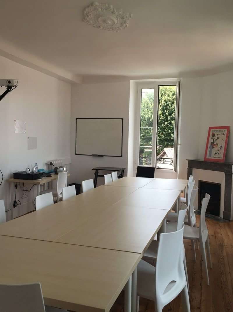 Klaslokaal voor taallessen met whiteboard, tafel en stoelen, licht interieur.