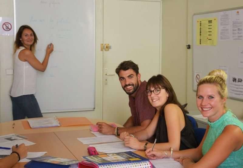 Een lerares geeft les aan drie studenten in een klaslokaal.