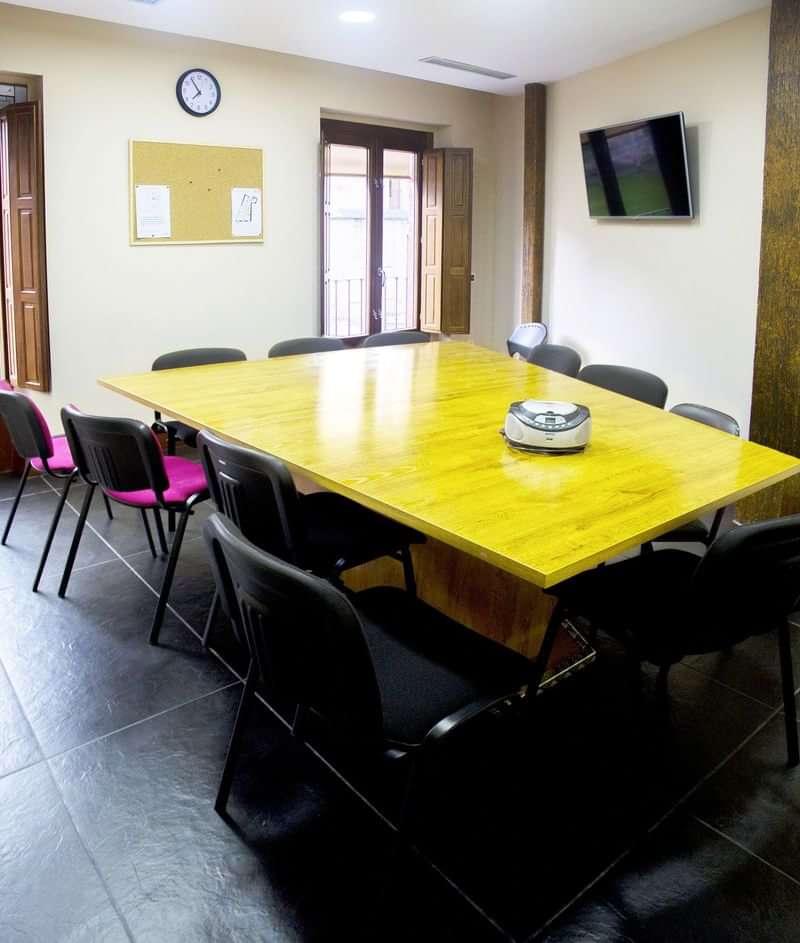 Language school classroom with table, chairs, clock, TV, and bulletin board.