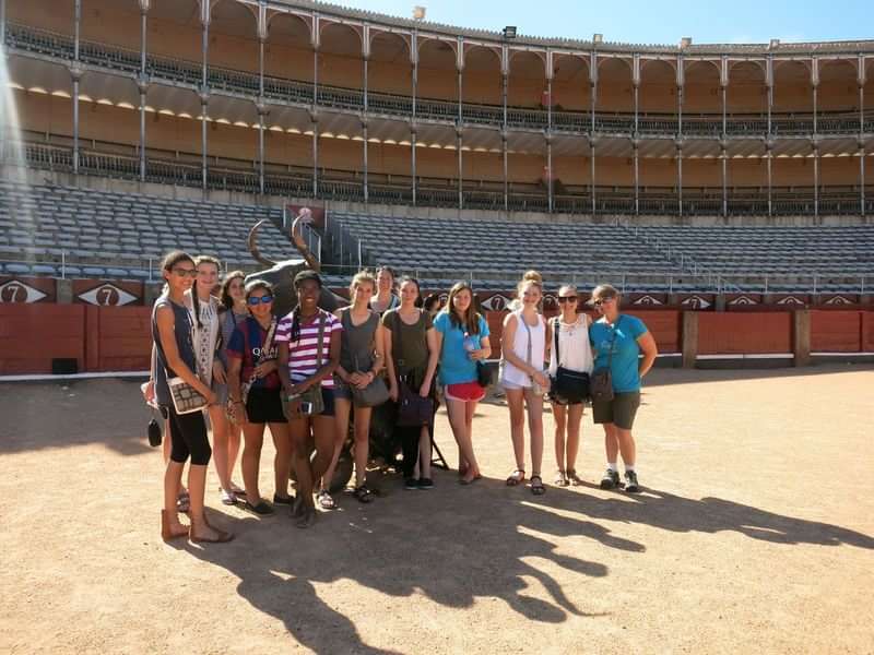 Students visiting a cultural landmark, possibly a bullring, during a language trip.