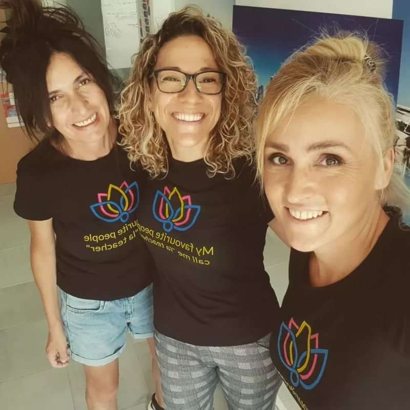 Three women smiling, wearing shirts promoting language learning or teaching.