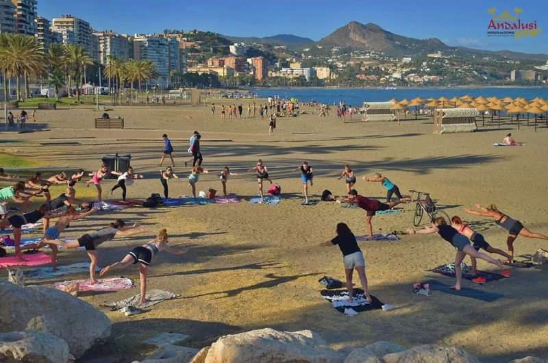 Beach yoga class with city and mountains in the background, promoting Andalusia.