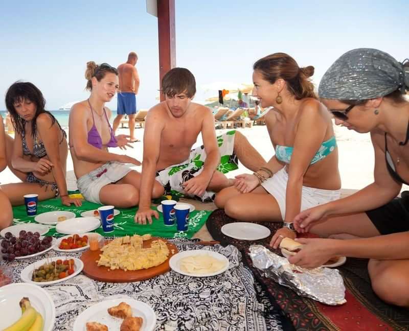 Groep vrienden geniet van een strandpicknick, ontmoeting tijdens taalreis.