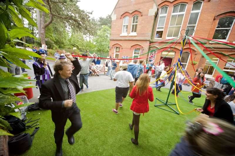 People celebrating, dancing, and interacting with a maypole in a festive scene.