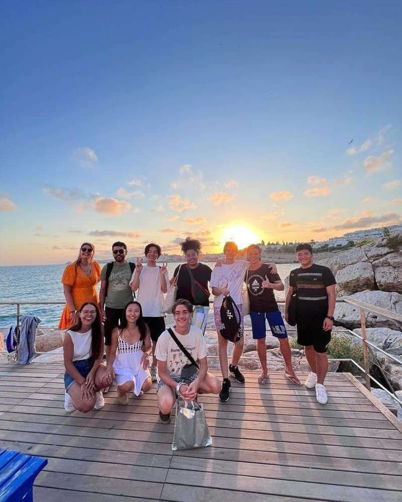 Groep vrienden geniet van een taalreis aan de kust bij zonsondergang.