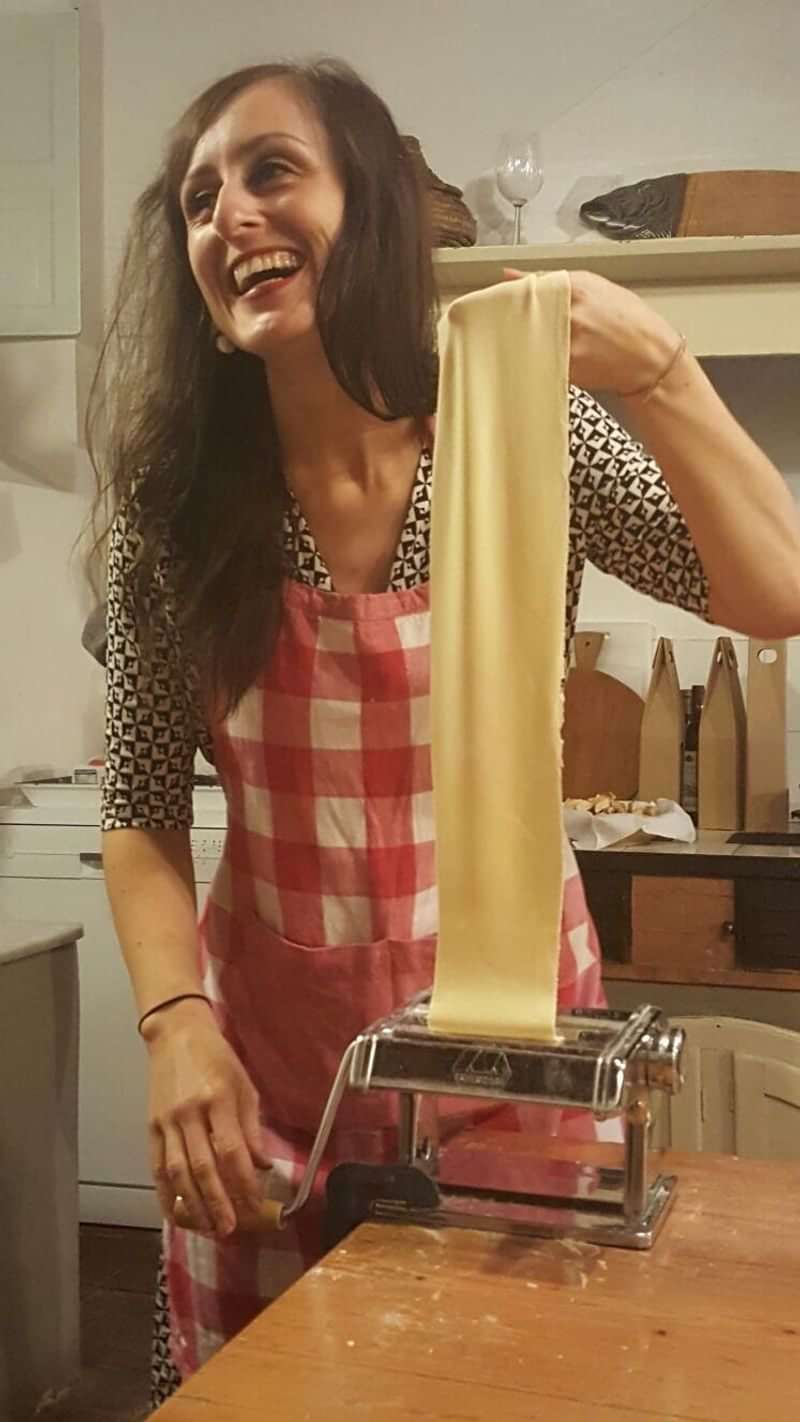 Person making pasta dough, wearing an apron, in a kitchen setting.