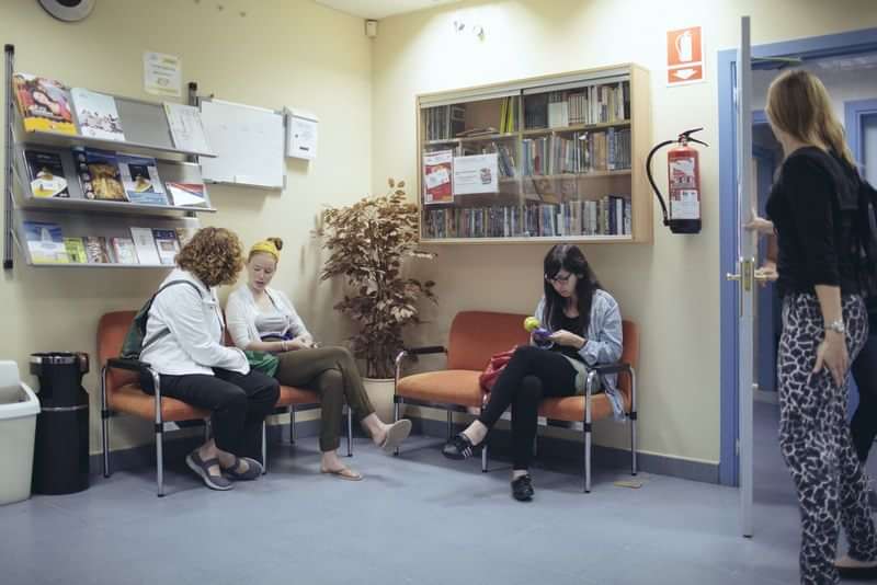 Students waiting in a language school lobby, reading books and chatting.