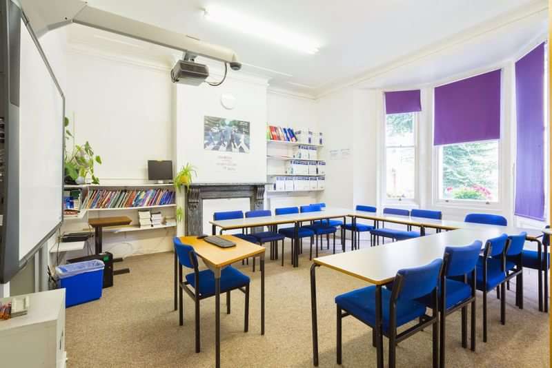 Language classroom with desks, chairs, projector, bookshelves, and large windows.