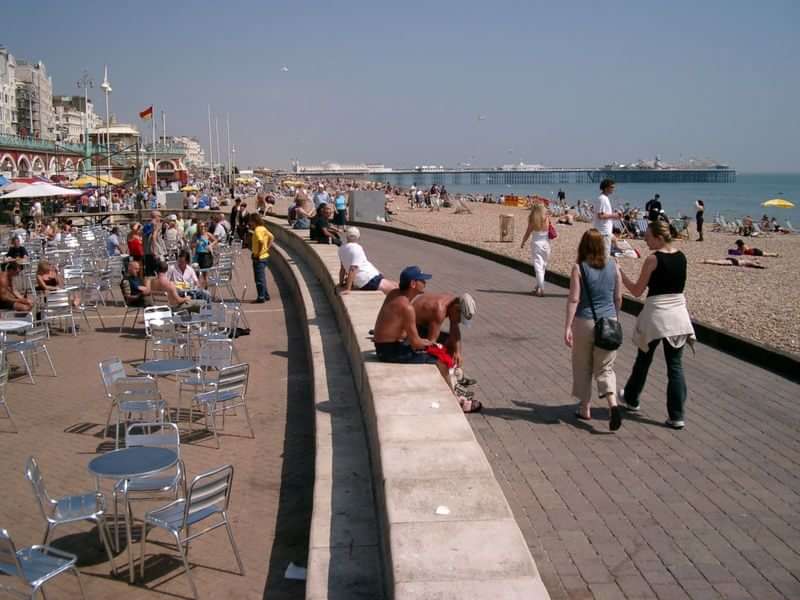 Bright beachfront with cafes, people strolling, sunbathing, and enjoying seaside.