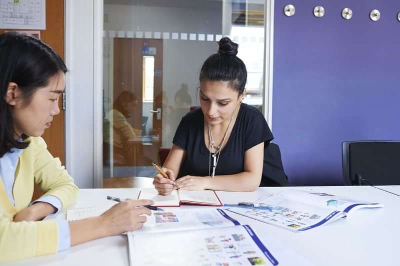 Two women studying language materials together in a classroom setting.