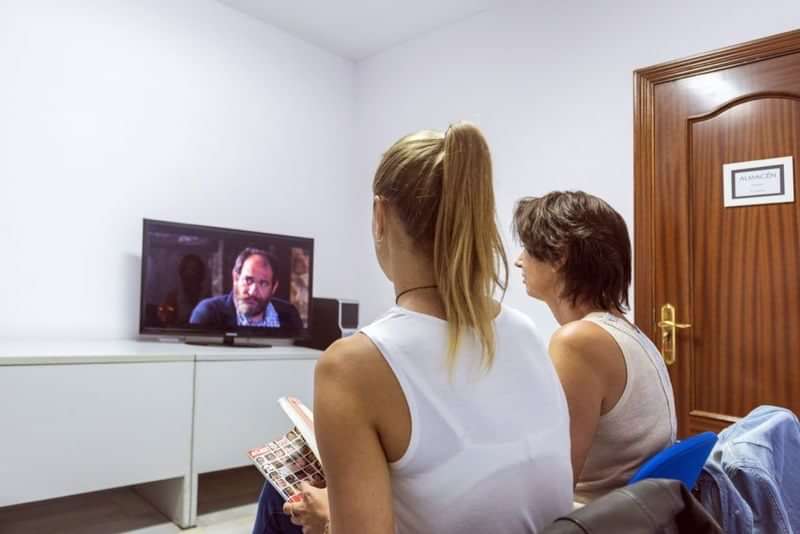 Twee mensen kijken tv en studeren een taalboek.